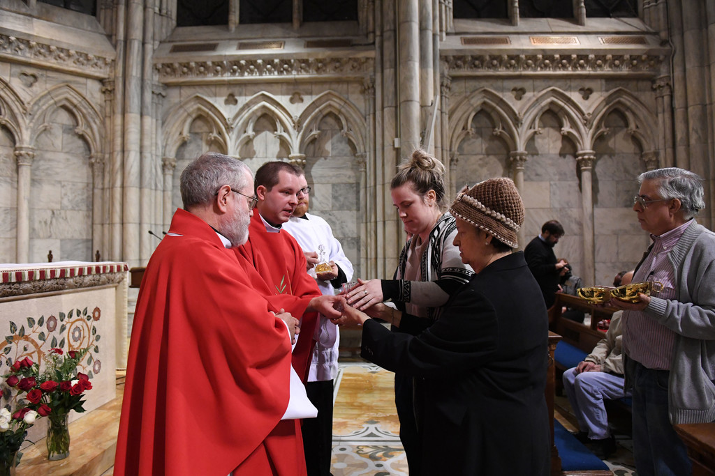 GIFTS—Father Jamie Dennis, who is blind, accepts the offertory gifts at the Mass he celebrated for the Feast of St. Lucy in the Lady Chapel of St. Patrick’s Cathedral. Presenting the gifts were Carmen Gomez and Richard Baldelli, who were assisted by Aisling Redican. At left is Father John Sheehan, S.J.