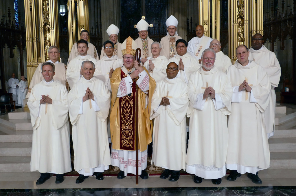 READY TO SERVE—The 12 new permanent deacons of the archdiocese gathered together after the Mass of Ordination. In the front row with Cardinal Dolan are, from left, Deacon Michael Sweeney, Deacon Carl Locatelli, Deacon Luis Abreu, Deacon James Cowan and Deacon John Hoey. In the middle row are Deacon Gregory Miller, Deacon Adhur Lekovic, Deacon Raymundo Masbad, Deacon Eymard Smith, Deacon Ivan Gemio, Deacon Bernard ‘Barney’ Kahn and Deacon Michel Hodge. In the back row are Deacon Francis Orlando, director of diaconate formation; Retired Auxiliary Bishop Josu Iriondo; Auxiliary Bishop John O’Hara, vicar for planning; Auxiliary Bishop Gerald Walsh, vicar for clergy; and Deacon James Bello, director of diaconate life and ministry.