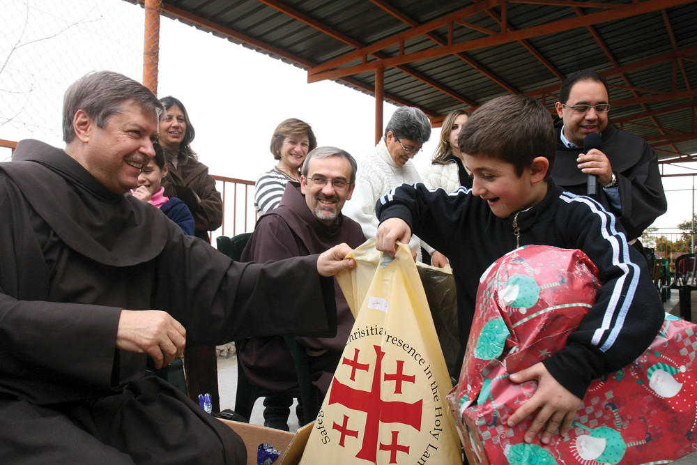 CHRISTMAS JOY—Father Peter Vasko, O.F.M., president of the Franciscan Foundation for the Holy Land, helps to distribute Christmas gifts at the foundation’s Bethlehem Boys Home.