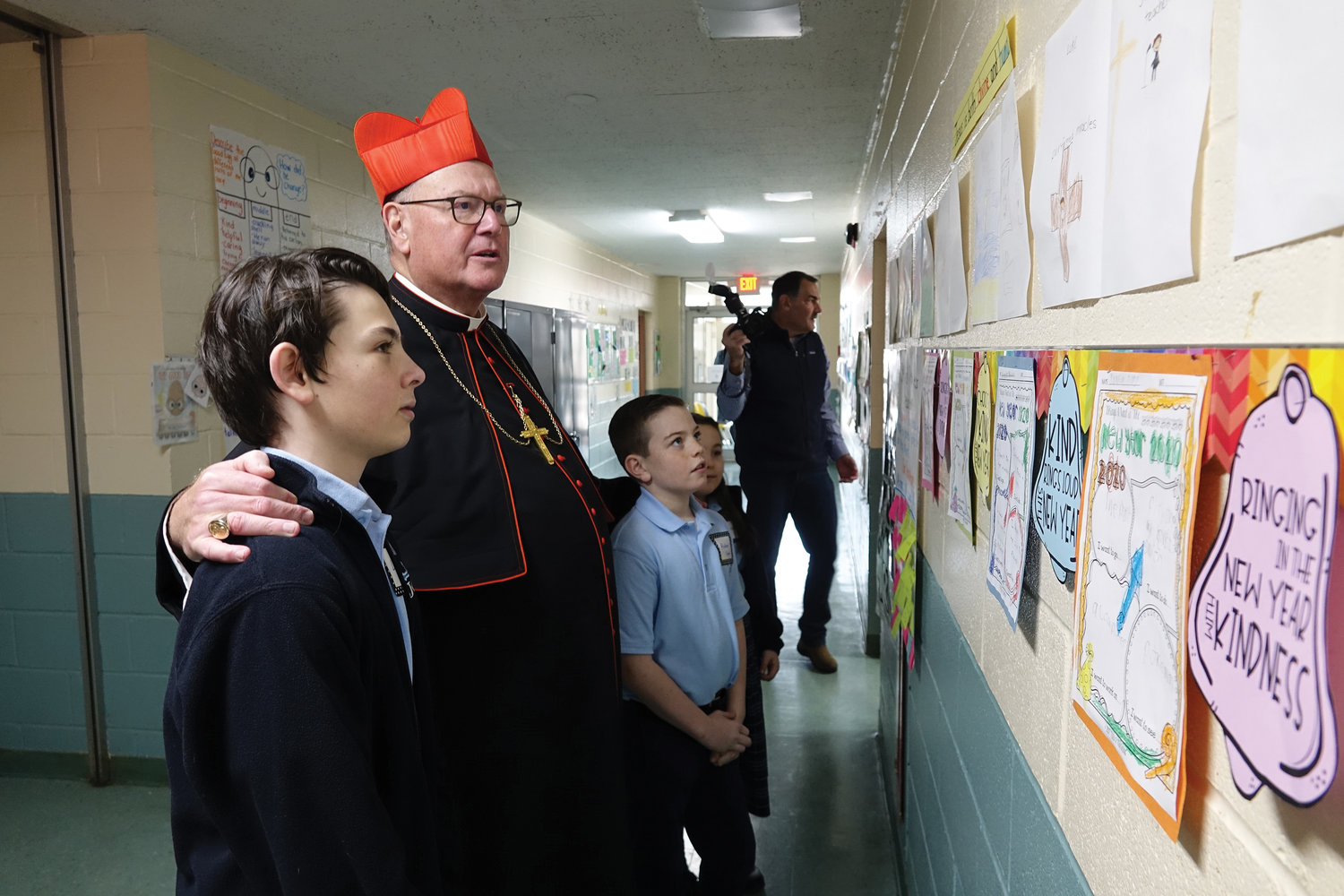 Cardinal Dolan, touring John Cardinal O’Connor School in Irvington Jan. 27, takes time to look at wall posters with Luke Hennisch, left, and Aiden Scholl. National Catholic Schools Week, the annual celebration of Catholic education in the United States, runs through Feb. 1.
