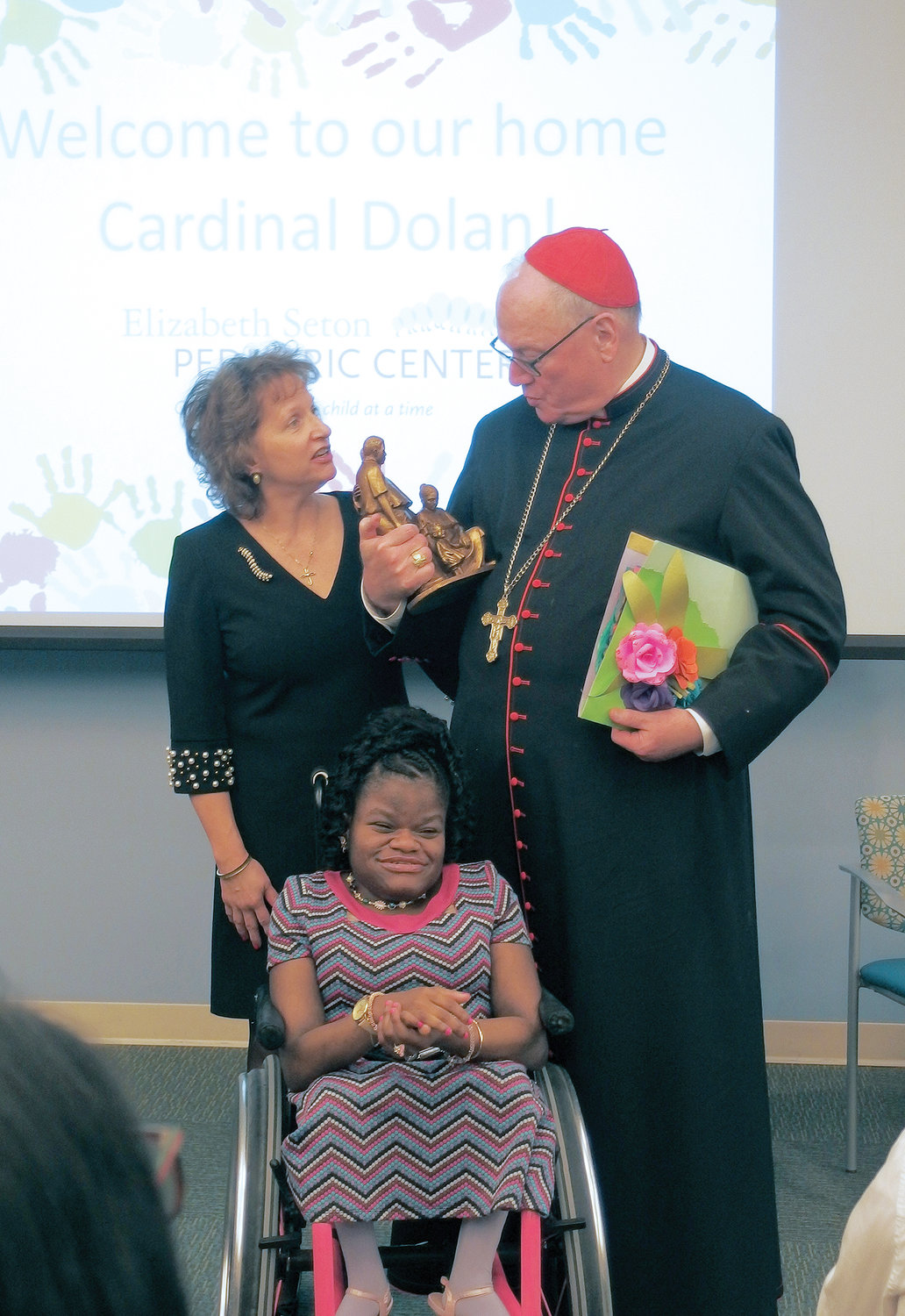 Cardinal Dolan speaks with Pat Tursi, CEO of Elizabeth Seton Children’s, during a visit to St. Elizabeth Seton Children’s Center in Yonkers last March. Seated in front of them is Stephanie, a resident. Elizabeth Seton Children’s Center received a $1 million grant from the Mother Cabrini Health Foundation to build a nursing facility for young adults who “age out” of pediatric care.