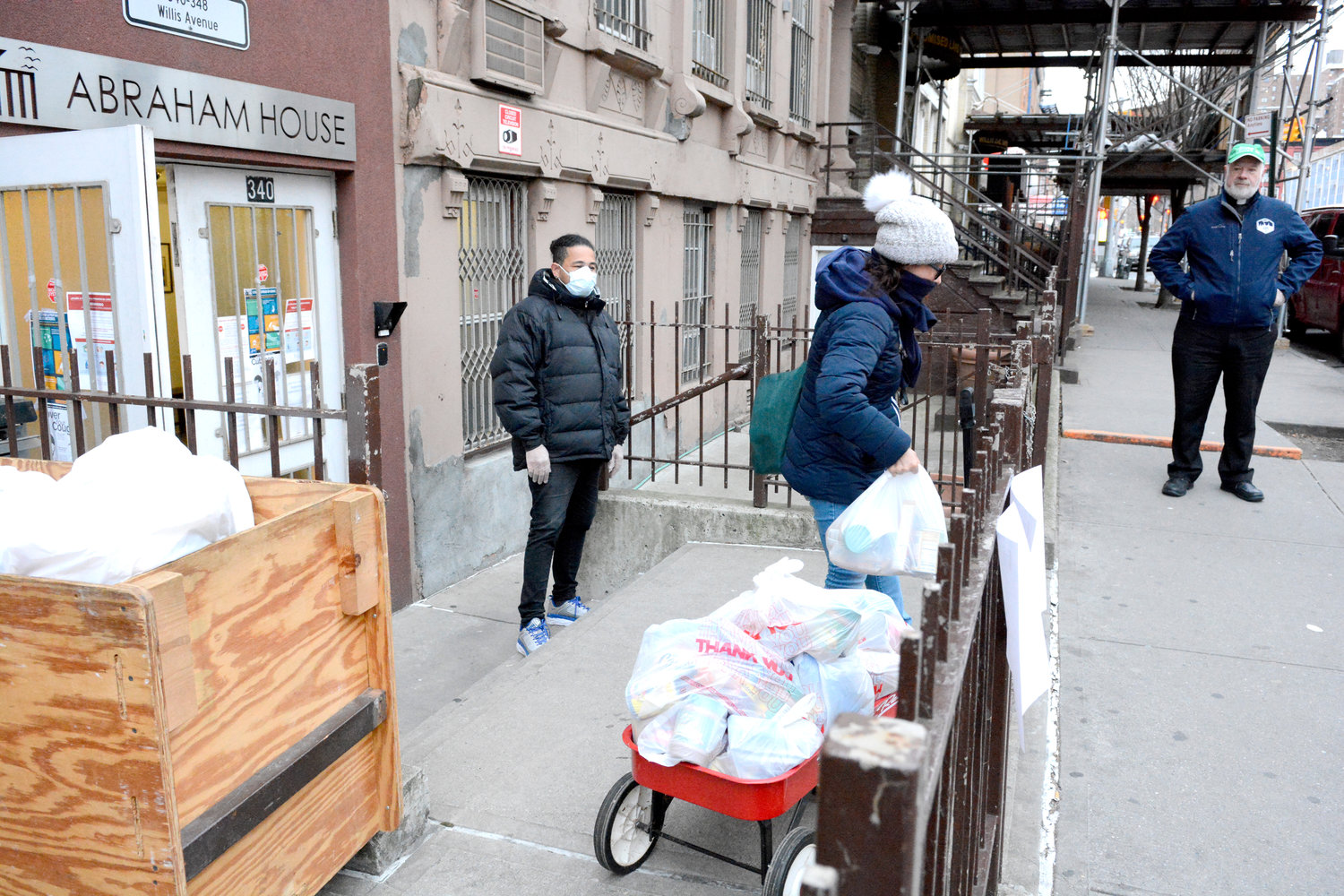 OUTSIDE PANTRY—A woman carries a bag of food outside Abraham House in the Bronx, where a “grab-and-go” pantry was set up March 21. Looking on from the sidewalk was Msgr. Kevin Sullivan, executive director of Catholic Charities. Residential assistant Andres Fernandez, wearing mask, maintains proper social distancing.
