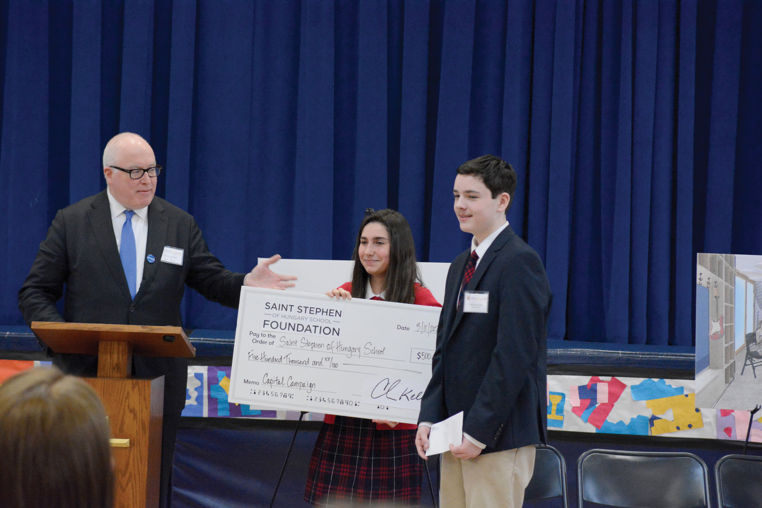 Foundation representative Christopher Kelly presents a ceremonial capital improvement check for the growing school, which is beginning a capital campaign to renovate the adjoining friary to accommodate increasing student enrollment. Construction to renovate preschool classrooms, the parking area and the school play yard is under way. Holding the check are eighth-graders Emily Carbone and Christopher Ganly.