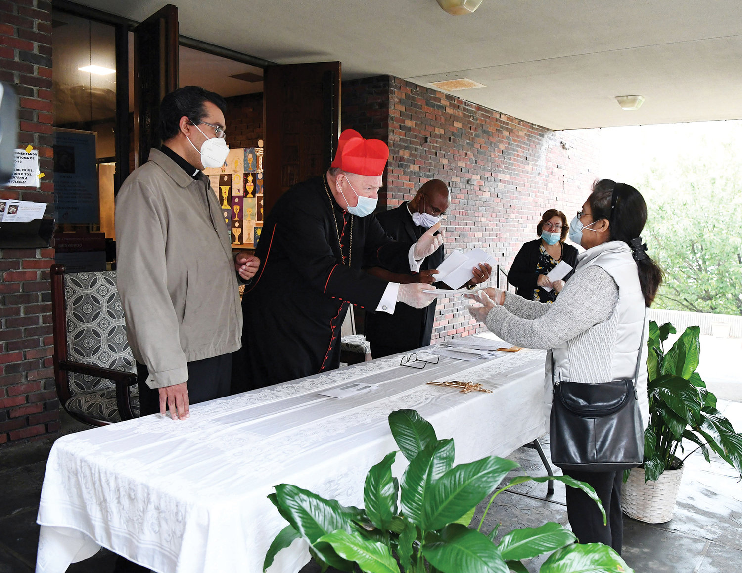Cardinal Dolan distributes a check to a woman at Our Lady of Good Counsel Church. On the left is Father Eric Cruz, Bronx director of Catholic Charities.