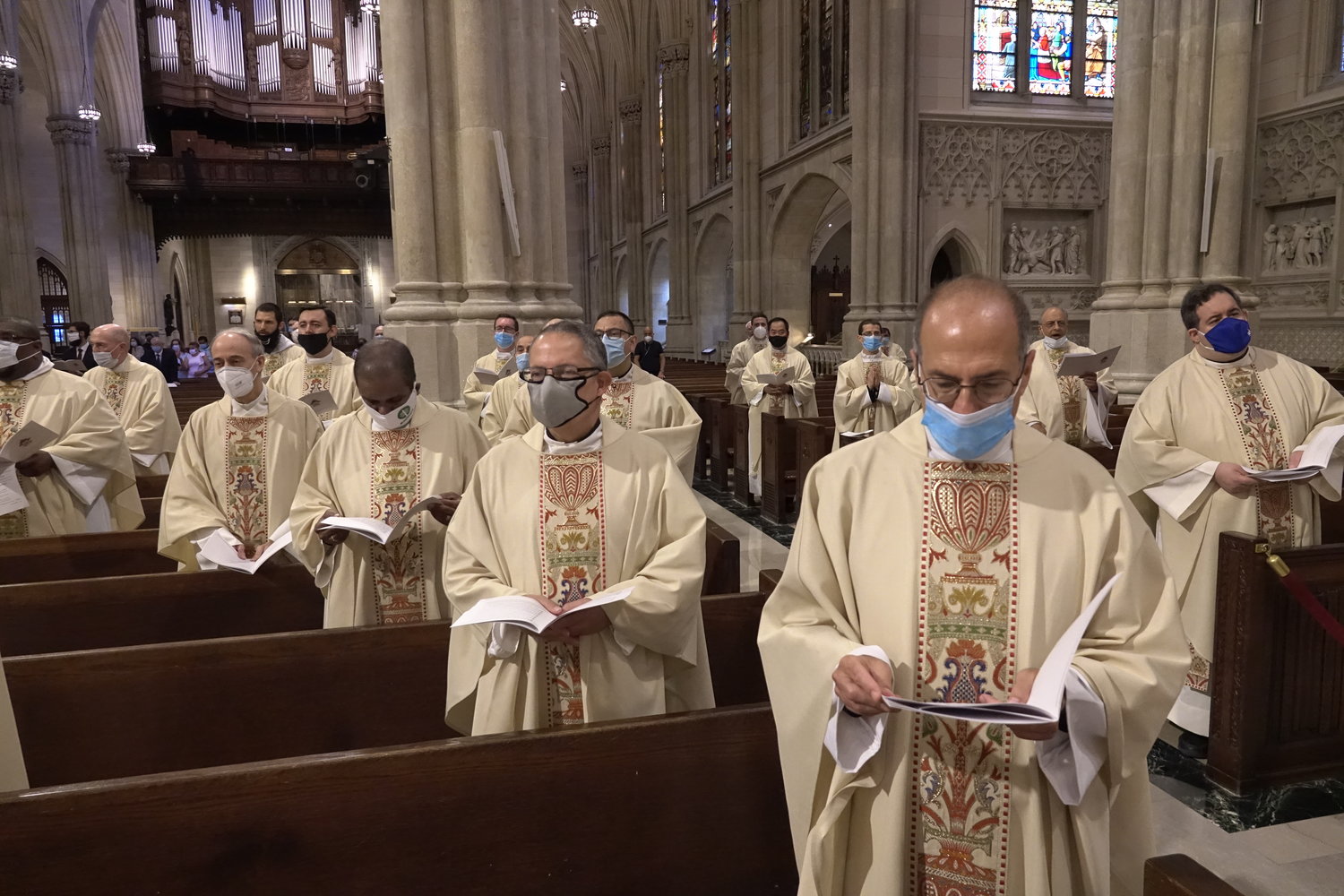 Priests, wearing protective face masks, follow their programs during the Mass of Ordination.