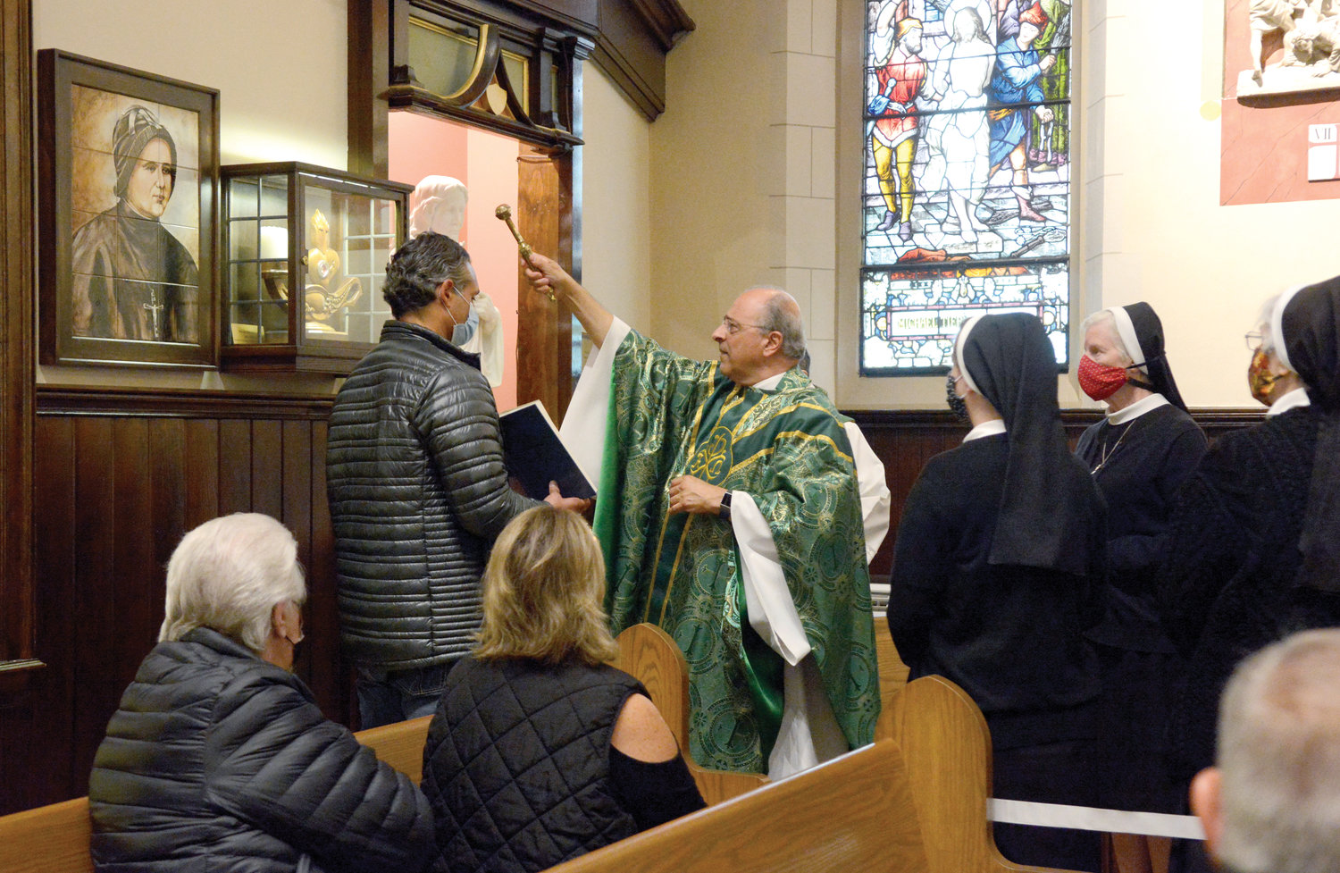 Father Anthony Sorgie, pastor of Immaculate Conception and Assumption of Our Lady parish in Tuckahoe, blesses a shrine to Blessed Clelia Merloni, foundress of the Apostles of the Sacred Heart of Jesus, during Vigil Mass he offered Oct. 17 at Immaculate Conception Church. Holding the Book of Blessings is Frank Musorrafiti, a captain of the Hartsdale Fire Department and parishioner of Sacred Heart, Hartsdale. He is a 1987 alumnus of the closed Sacred Heart Private School on Zerega Avenue in the Bronx, where Blessed Clelia’s congregation served. Sister Barbara Thomas, A.S.C.J., provincial superior of the U.S. Province of the Apostles of the Sacred Heart of Jesus in Hamden, Conn., is at front, red mask.