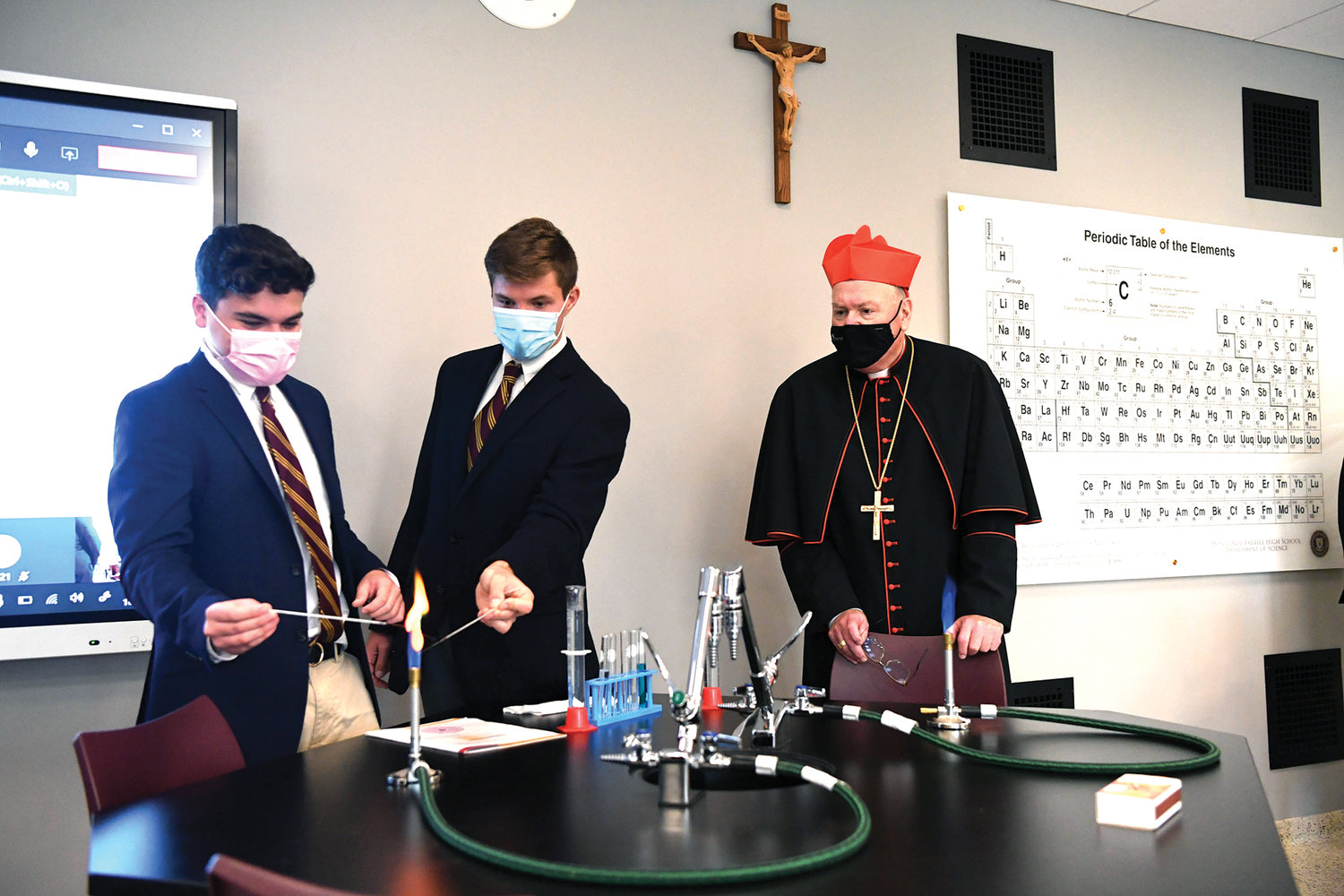 Cardinal Dolan watches as students Eddie Morales and James Moore work on a chemistry experiment.