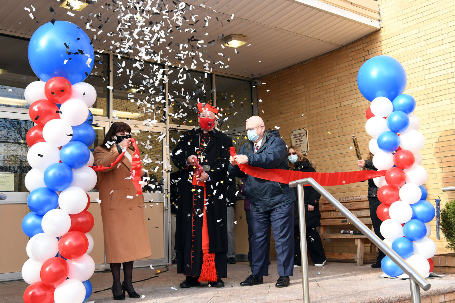 Cardinal Dolan cuts the ribbon at the dedication, assisted by Zoilita Herrera, regional superintendent of Staten Island Catholic schools, left, and Michael Deegan, superintendent of schools in the archdiocese, right.