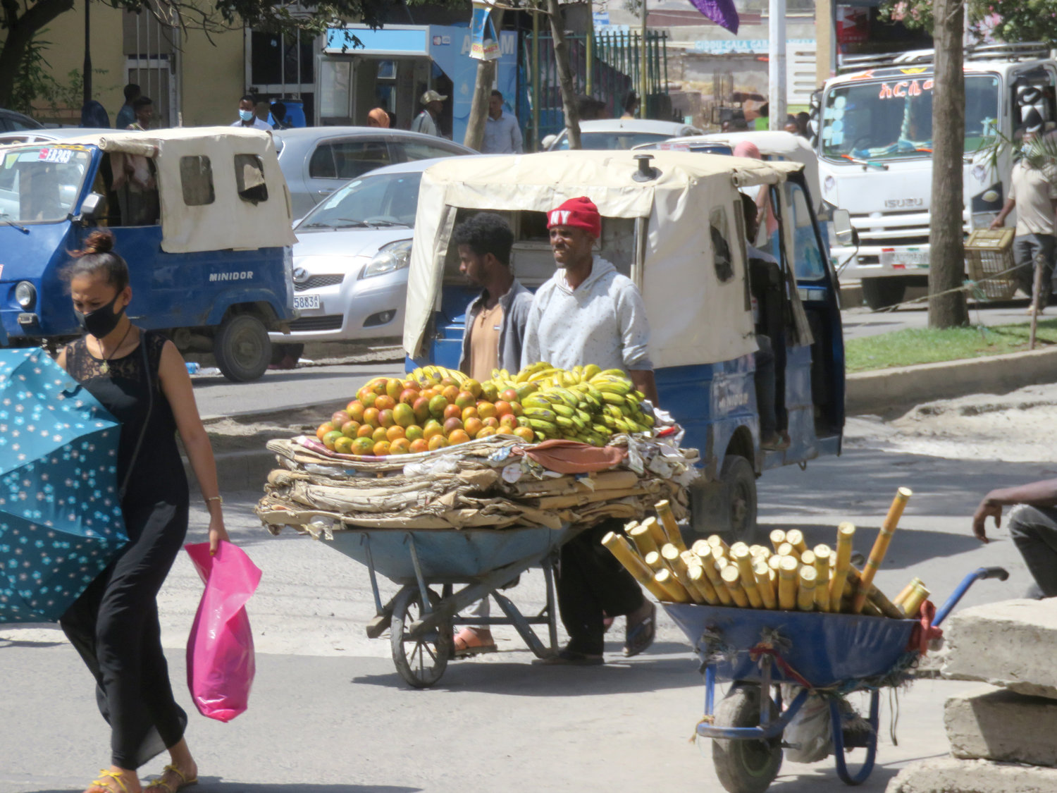A local vendor wearing a New York hat pushes a cart with fresh produce.