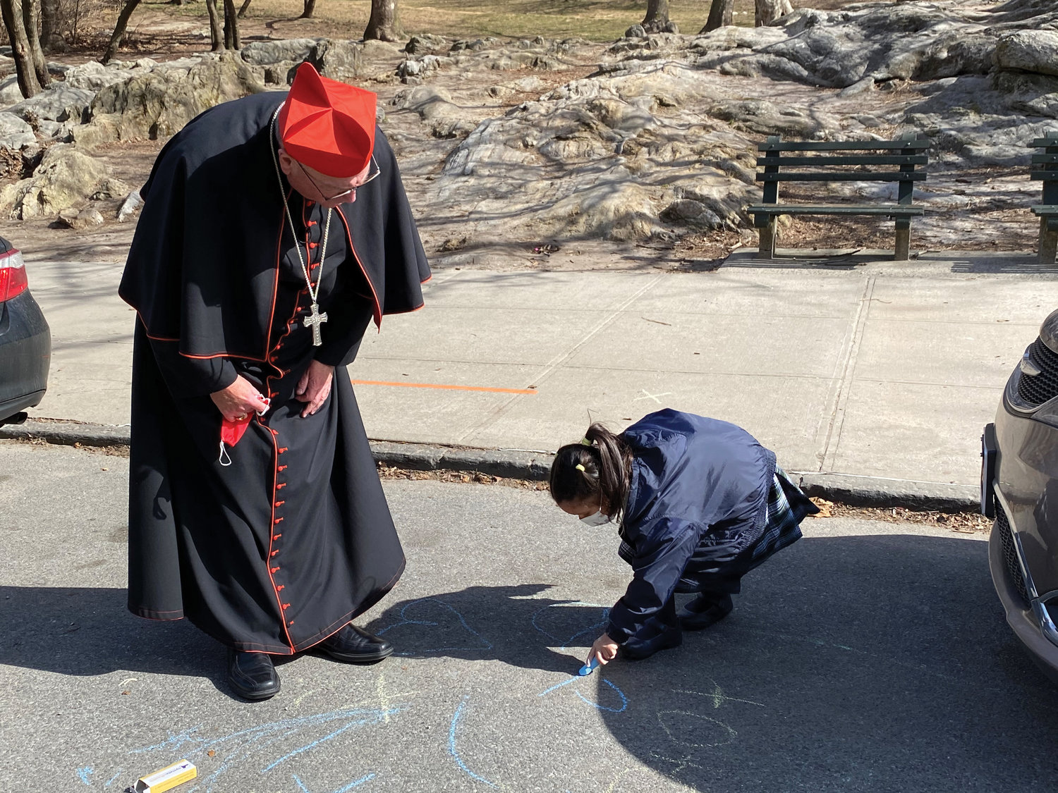 Kindergarten student Chloe Rana writes with chalk outside the school as Cardinal Dolan looks on.