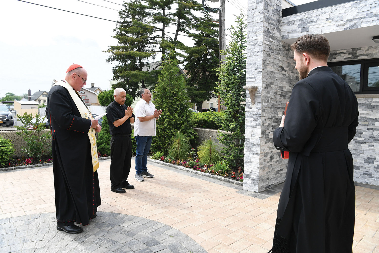 Cardinal Dolan leads a prayer of invocation and reparation on the plaza of Our Lady of Mount Carmel-St. Benedicta-St. Mary of the Assumption parish on Castleton Avenue on Staten Island May 22. The empty ledge in the brick facade is where the statue of Our Lady of Mount Carmel was before it was destroyed by a vandal. Next to Cardinal Dolan is Father Hernan Paredes, S.J., pastor; Abelardo Aleman, a trustee of the parish; and at front right, Father Stephen Ries, priest secretary to Cardinal Dolan.