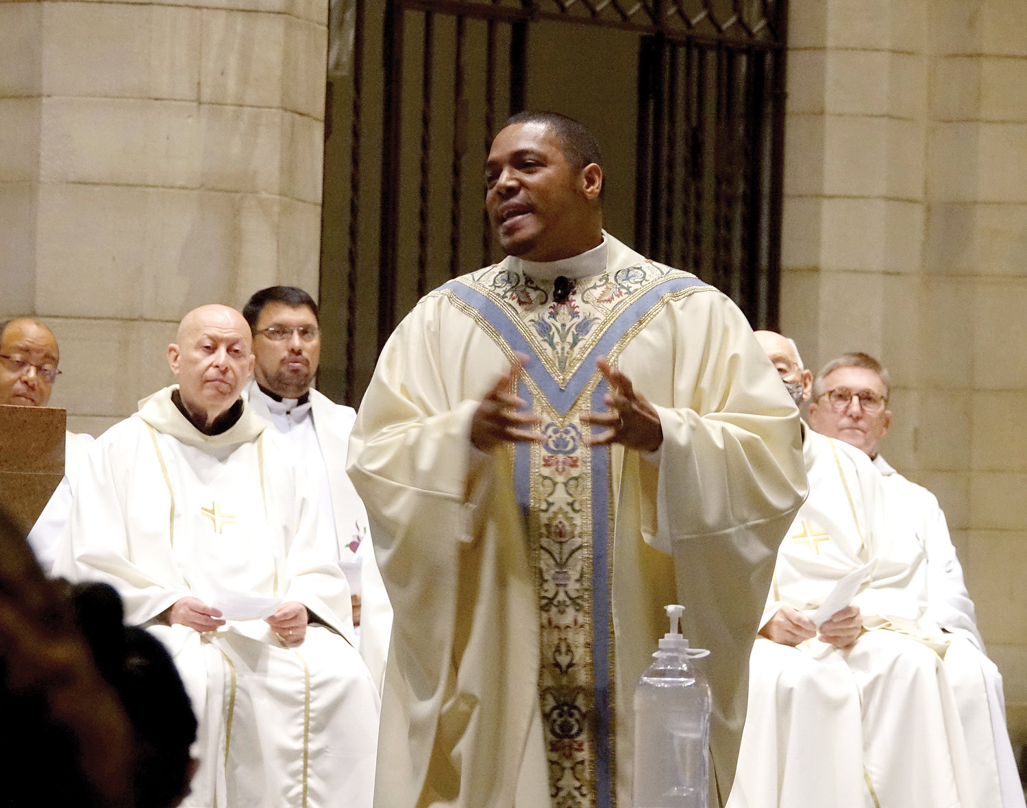 El padre Contreras predica su homilía con otros sacerdotes detrás de él.