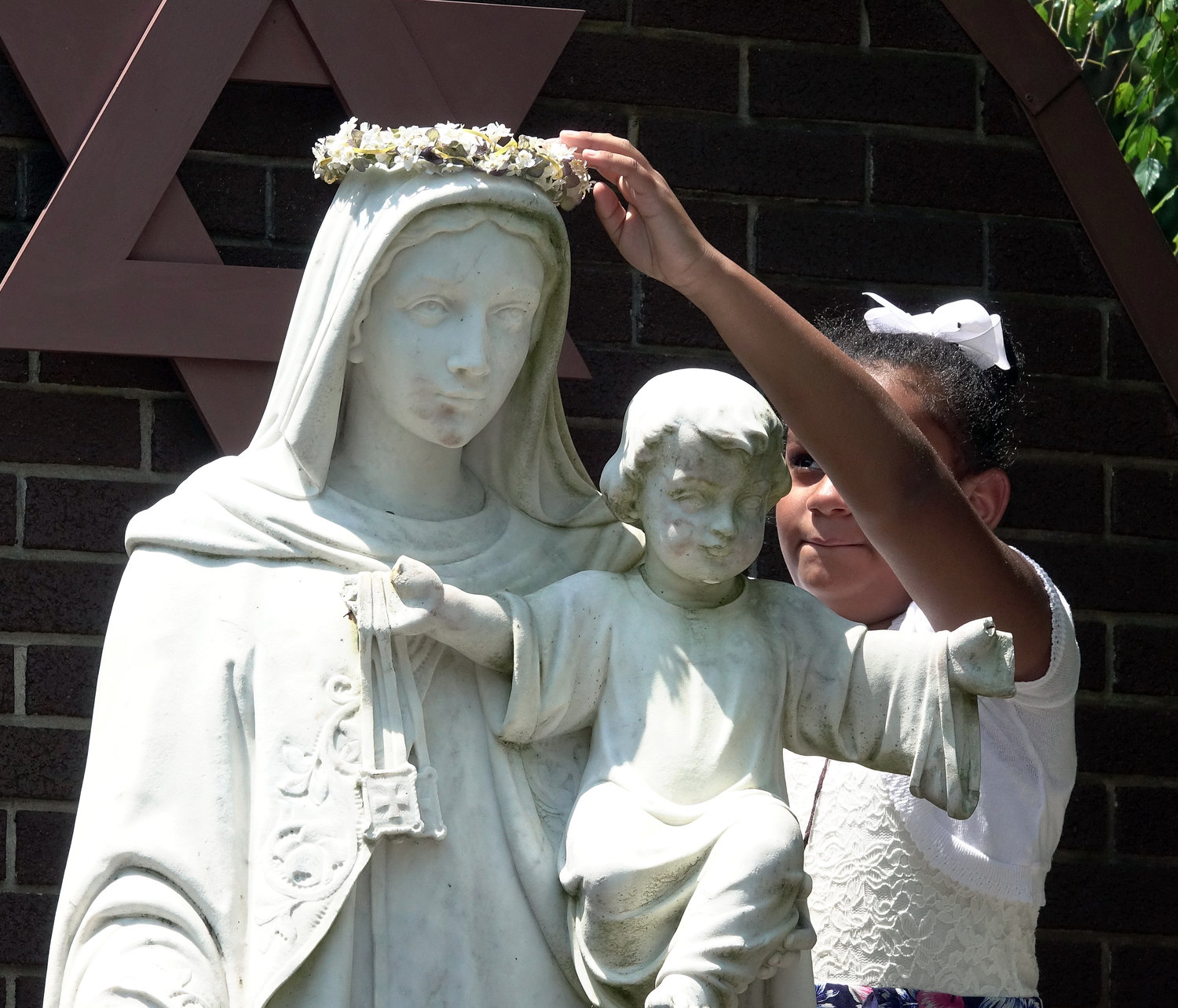 A girl crowns a statue of the Virgin Mary July 16, the feast of Our Lady of Mount Carmel, outside the National Shrine of Our Lady of Mount Carmel in Middletown. Women pray during the Mass.