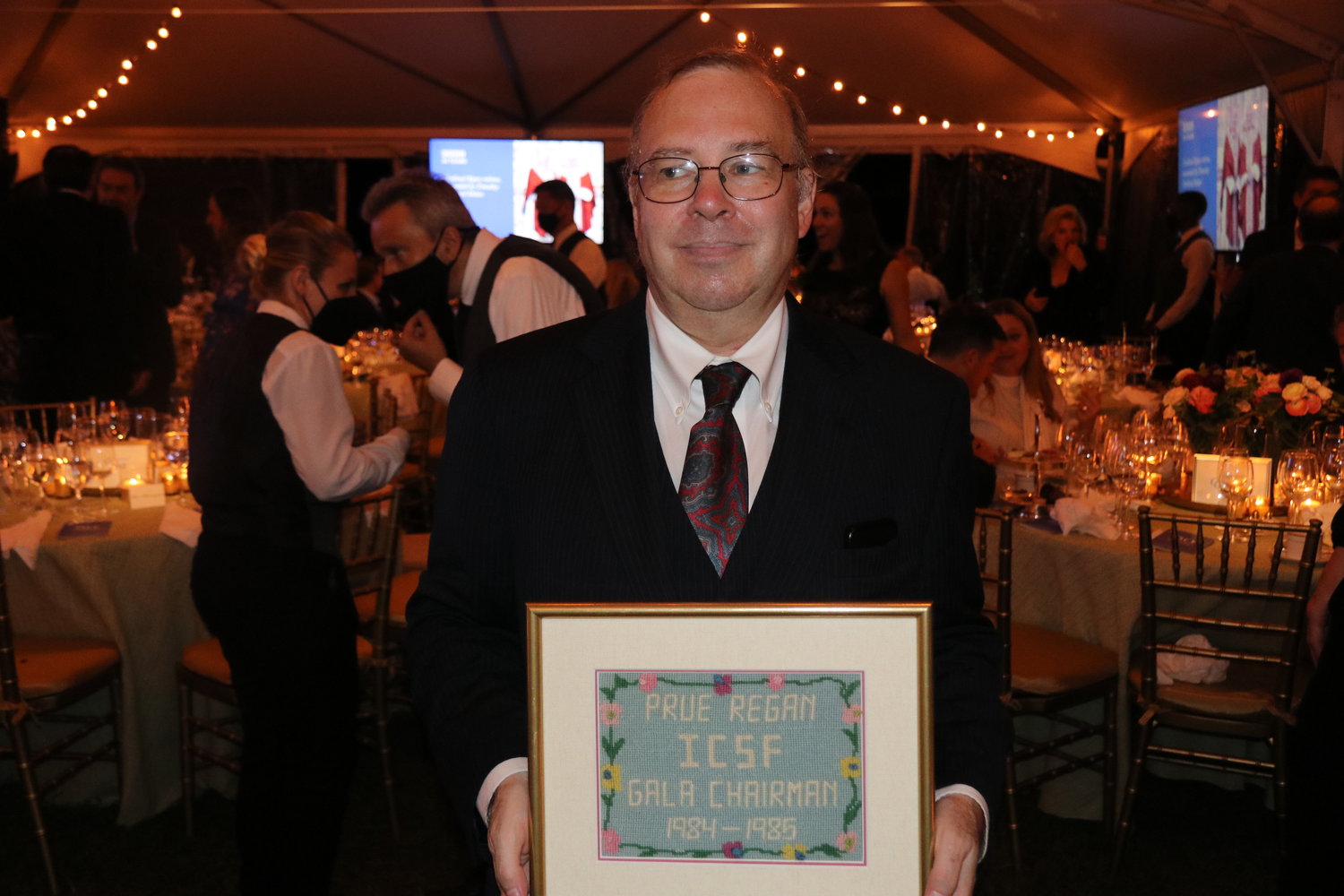 William Regan, at the Inner-City Scholarship Fund 50th anniversary gala, holds a framed needlepoint recognizing the service and support of his late mother, Prudence (Prue) Regan, to ICSF.