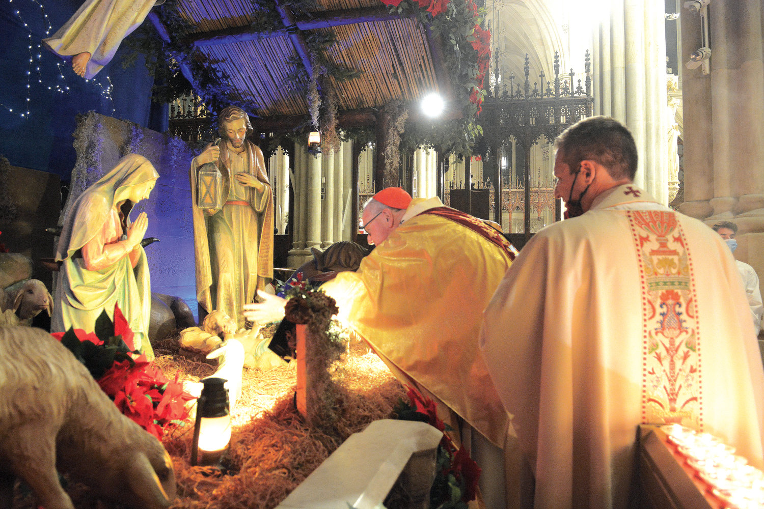 O HOLY NIGHT—Cardinal Dolan gently places a statue of the Infant Jesus in the creche at St. Patrick’s Cathedral during Christmas Midnight Mass Dec. 25. Father Enrique Salvo, cathedral rector, left, carried the statue in the procession before handing it to the cardinal in front of the creche.