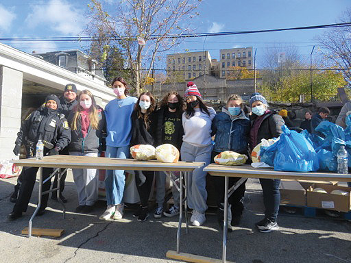 CRS Club members participate in the Thanksgiving Food Drive at the St. Peter-St. Denis parish food pantry in Yonkers alongside two Yonkers police officers at far left and, at far right, CRS Club adviser Dr. Valerie Torres.