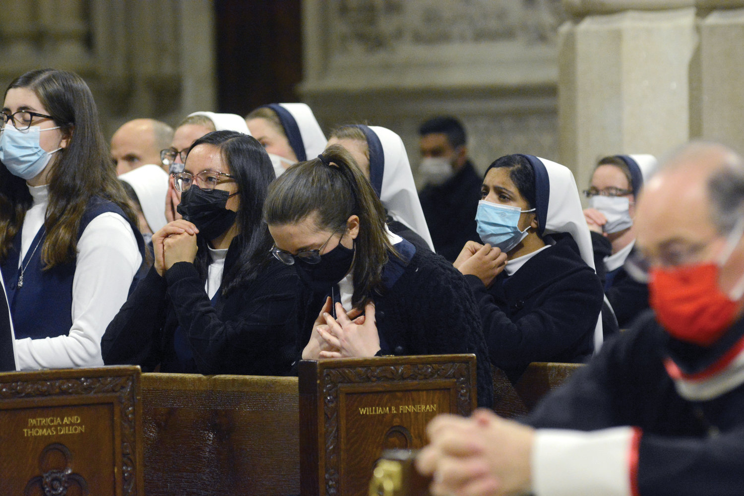 A postulant with the Sisters of Life clutches her heart in prayer. A man and a woman pray in a pew.