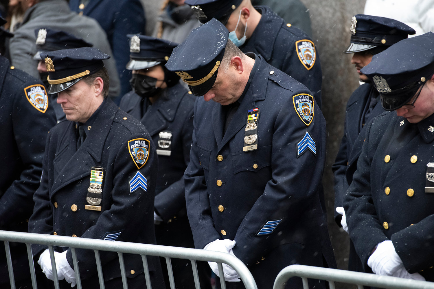 Police officers, with snowflakes on their caps and jackets, bow their heads outside St. Patrick’s Cathedral Jan. 28