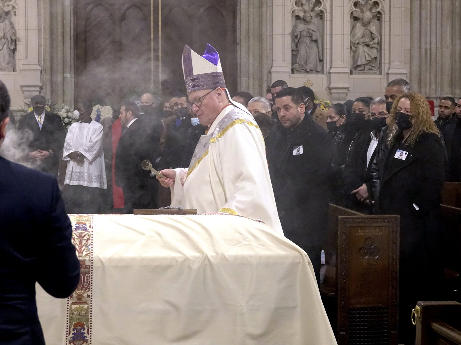 Cardinal Dolan sprinkles holy water on the casket.