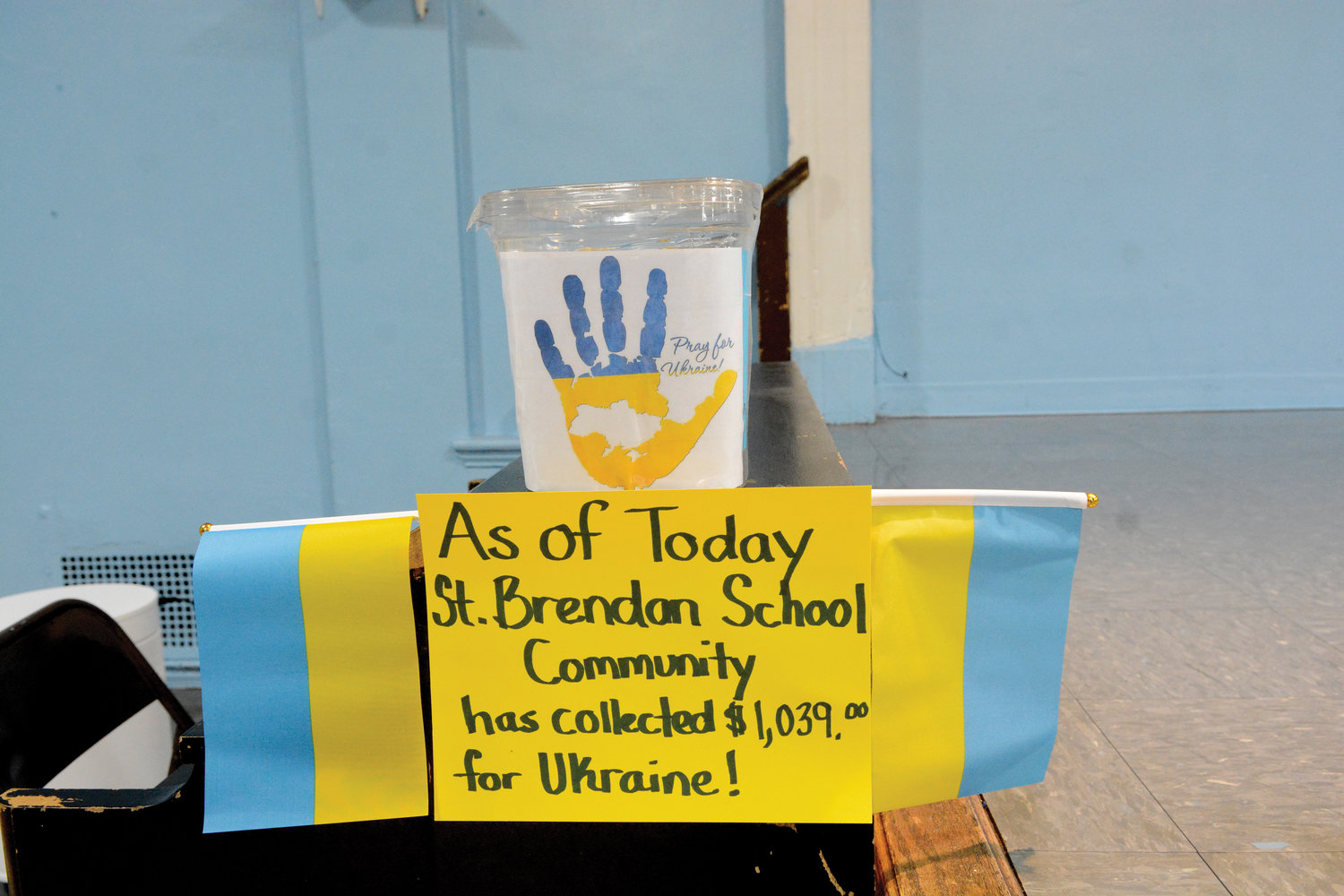 A poster below a collection container, flanked by Ukrainian flags, displays the total St. Brendan’s School has contributed to the cause so far.