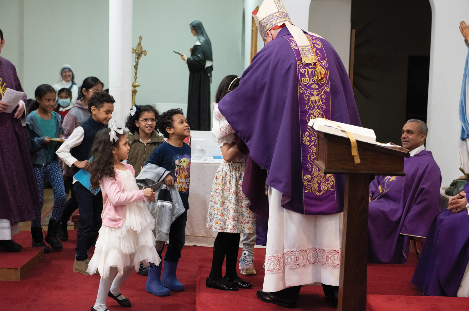 El cardenal Dolan recibe regalos de niños alegres después de la misa que él celebró. Los niños hicieron dibujos de Beato Carlo para la ocasión.