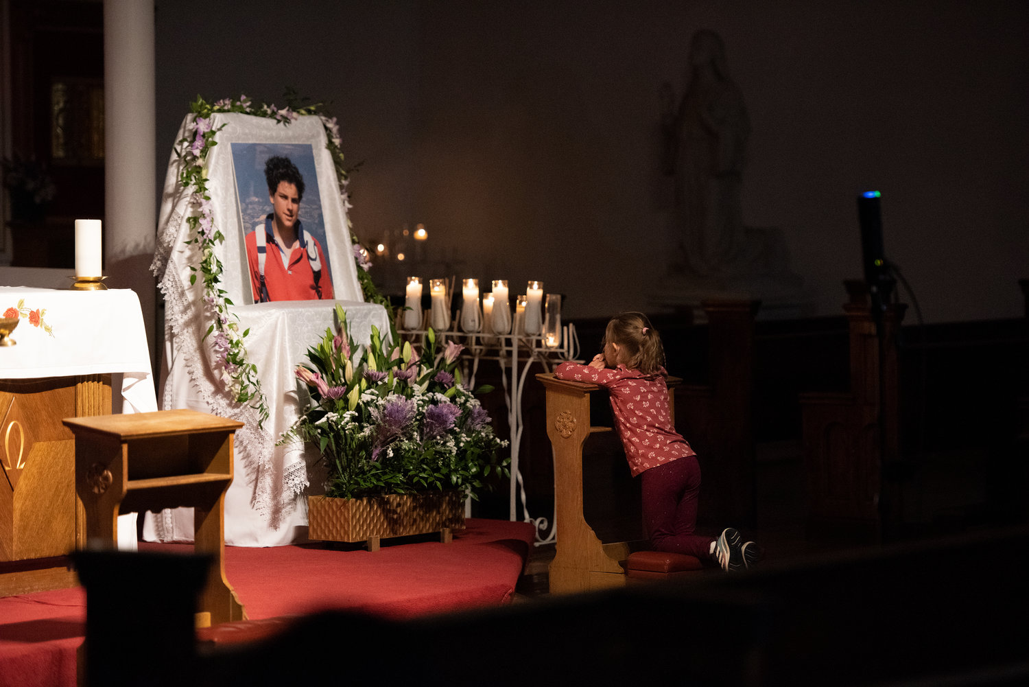 A little girl prays before an image of Blessed Carlo Acutis, top, during an evening gathering April 7 featuring Holy Hour, Mass and veneration at St. Rita of Cascia Church in the Bronx.