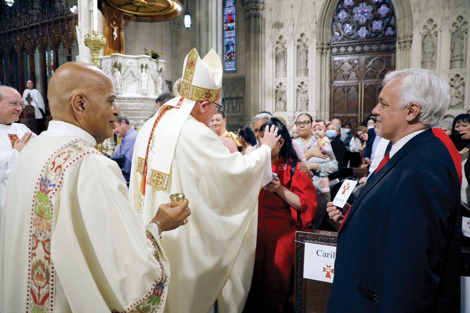 Cardinal Dolan receives assistance from Joe Long, right, director of children’s faith formation, at the Confirmation Mass for Young People with Special Needs last month at St. Patrick's Cathedral. Also shown is Deacon James Bello.