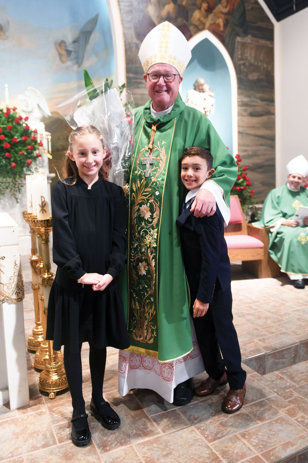 Katherine Campbell and Samuel Caxon from the Sacred Heart-Our Lady of Pompeii religious education program present flowers to Cardinal Dolan at Our Lady of Pompeii Church Oct. 1.