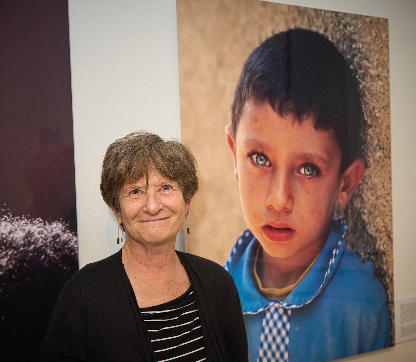 Photographer Ilene Perlman, who had three photos in the show, stands near an image of a little boy in Smakieh, Jordan, taken by Miriam Sushman.